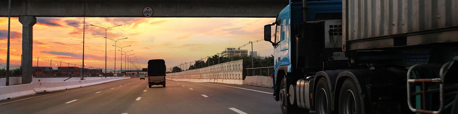 Semi truck going under an interstate bridge at sunset